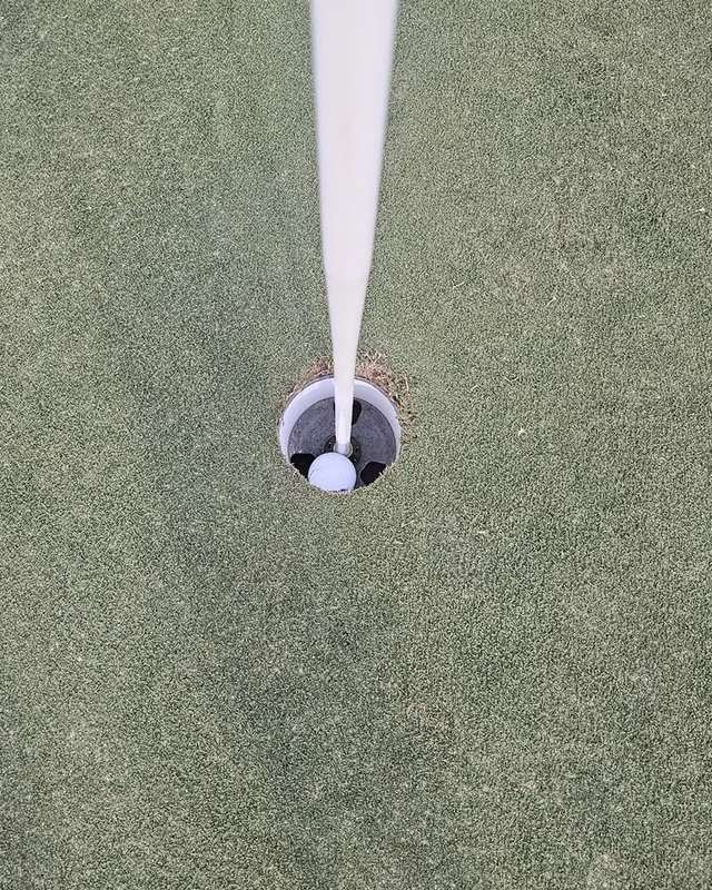 Looking straight down the flagstick: a white golf ball sitting at the bottom of the hole.
