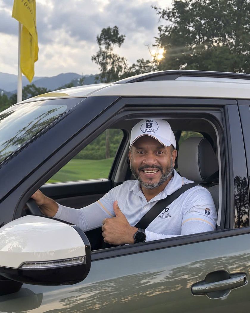 Mario in the driver’s seat of his new car, seatbelt fastened, grinning, thumb up out of the window.